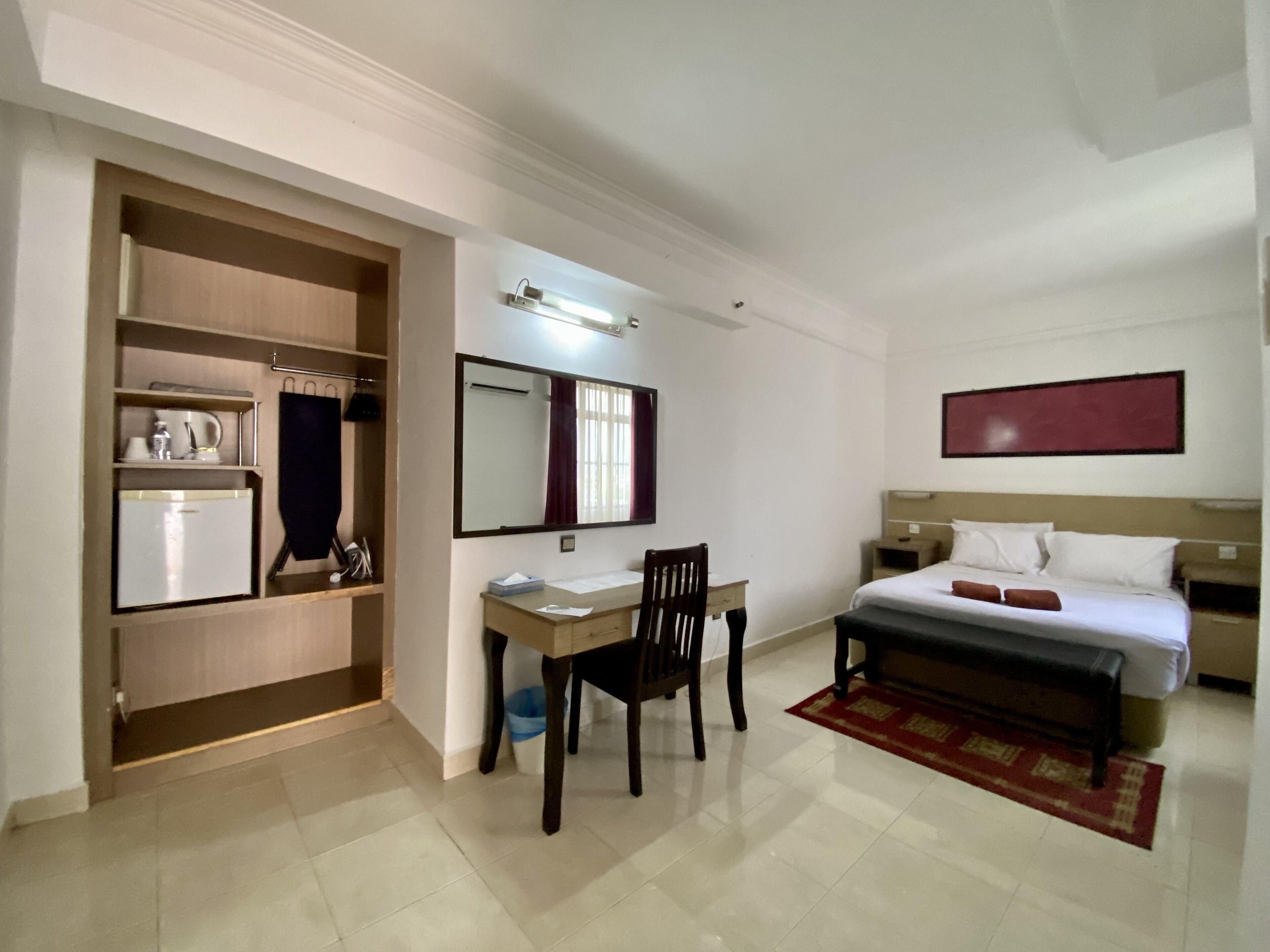 Een hotelkamer met een bed, een bureau, een stoel, een kledingkast en een spiegel.