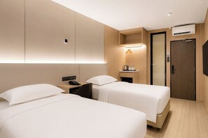 A hotel room with two beds, a desk with a telephone, a bedside table with a lamp, and a wardrobe with an air conditioning unit. - Ming Star Hotel (Kuala Terengganu)