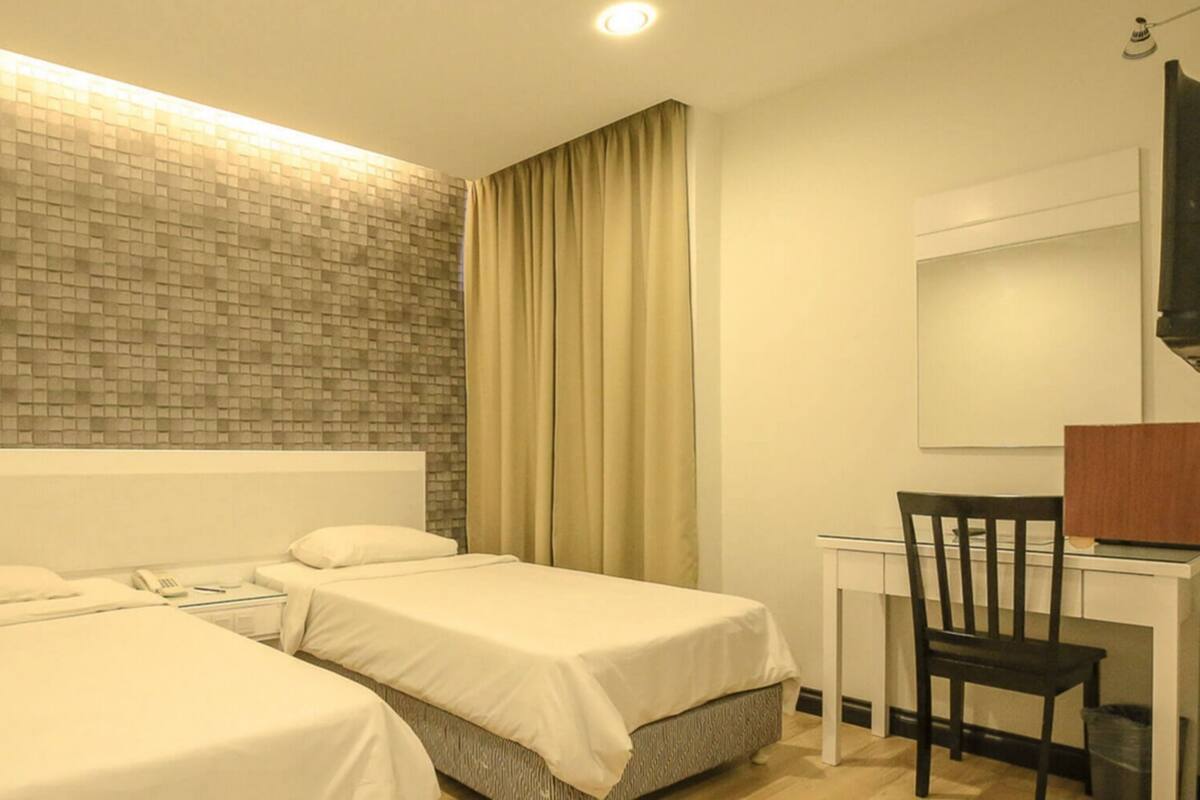 A hotel room with two beds, a desk, a chair, a mirror, and a brick-patterned wall.