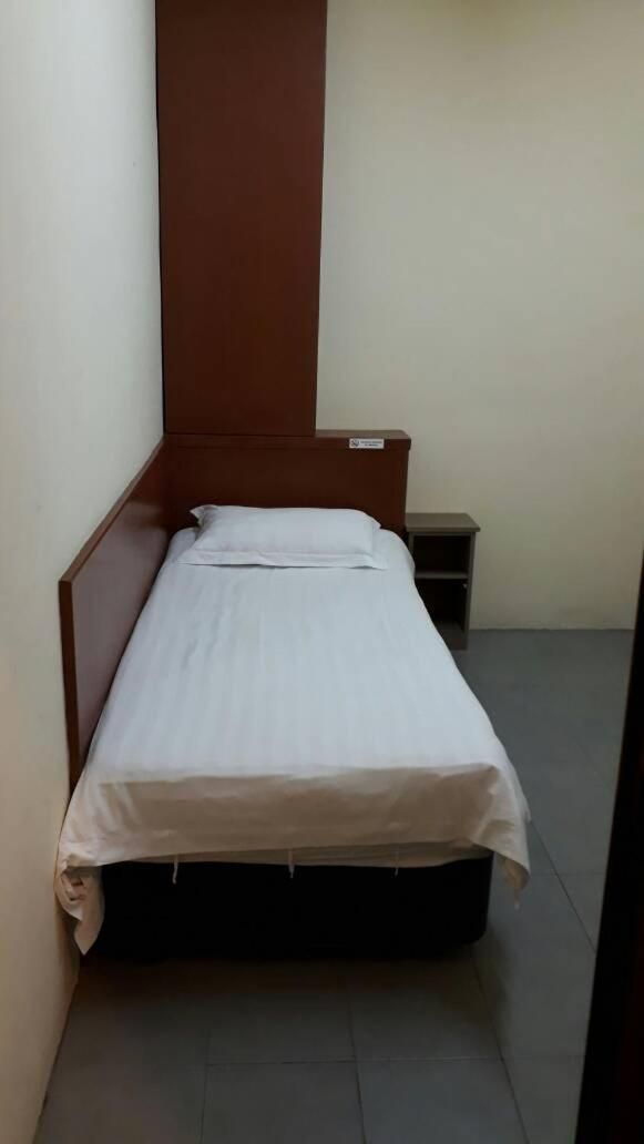 A small, single-bed room with a wooden headboard, a bedside table, and a nightstand.
