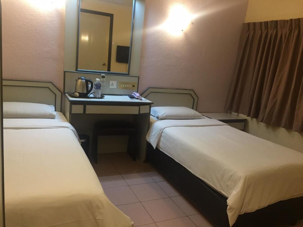 Une chambre d’hôtel avec deux lits simples, un bureau avec une chaise, un miroir et une lampe fixée au mur.