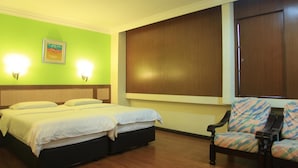 A hotel room with two beds, a green wall, a large window with wooden blinds, and a chair with a colorful pattern. - The Inn Hotel (Kuala Terengganu)