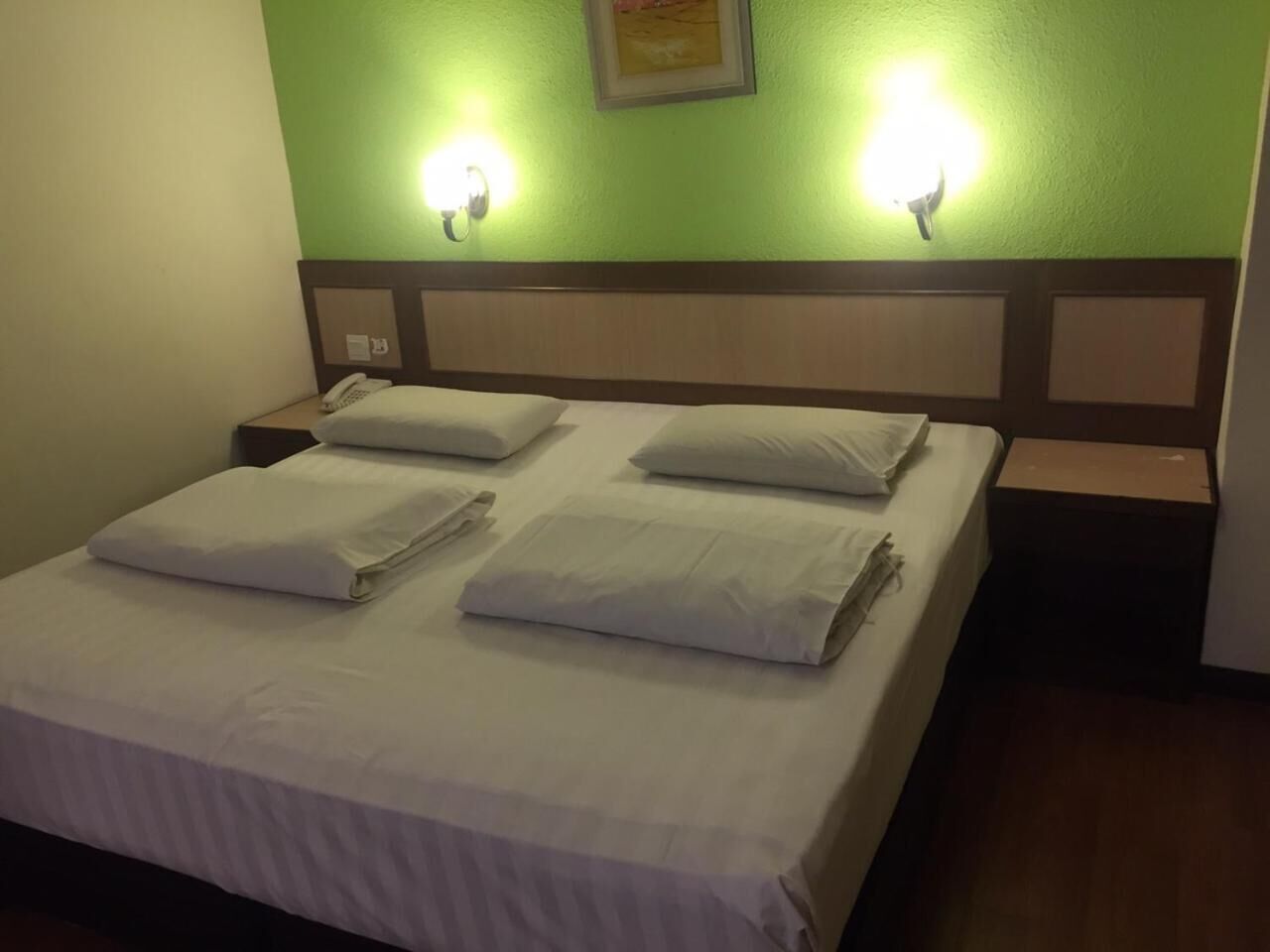 A neatly made bed with white linens and pillows, two bedside lamps, and a green wall with a framed picture.
