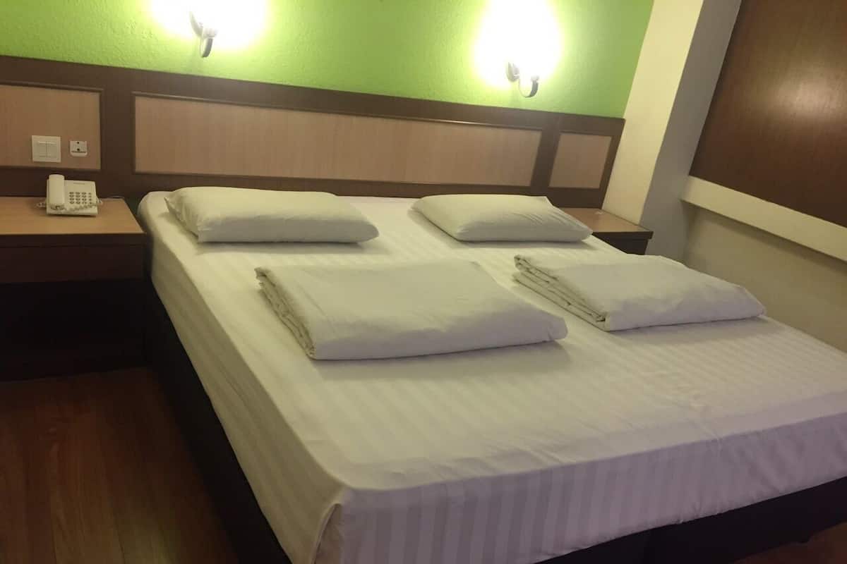 A hotel room with a bed, two pillows, a bedside table with a phone, and a wall-mounted light.
