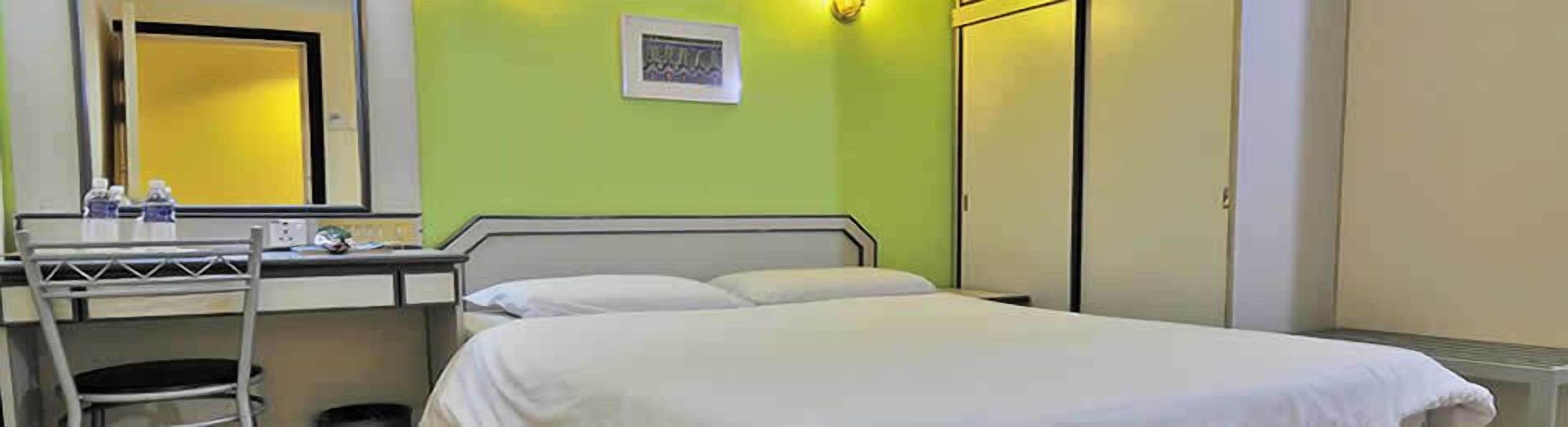 A hotel room with a bed, a desk with a chair, a mirror, and a wardrobe.