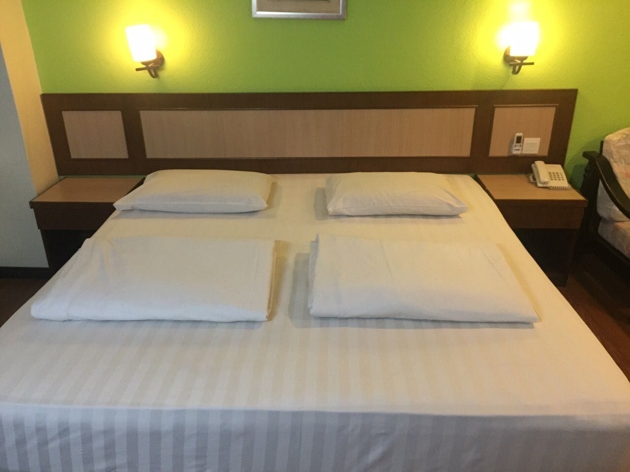 Cama bem arrumada com travesseiros e mesa de cabeceira com telefone e bloco de notas.