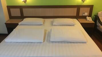Cama bem arrumada com travesseiros e mesa de cabeceira com telefone e bloco de notas.