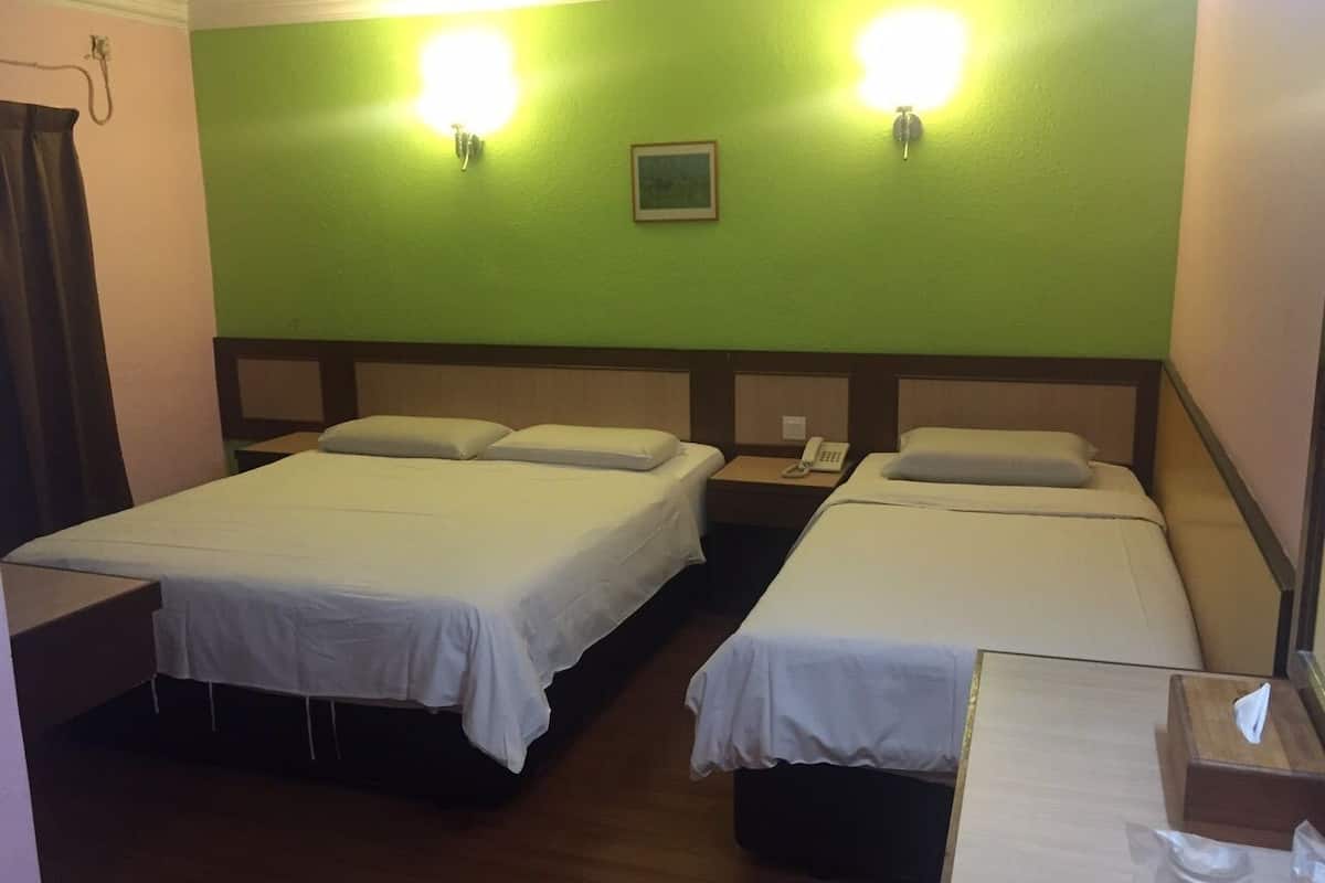A hotel room with two single beds, a bedside table with a lamp, a small bedside table with a phone, and a green wall with two wall-mounted lights.