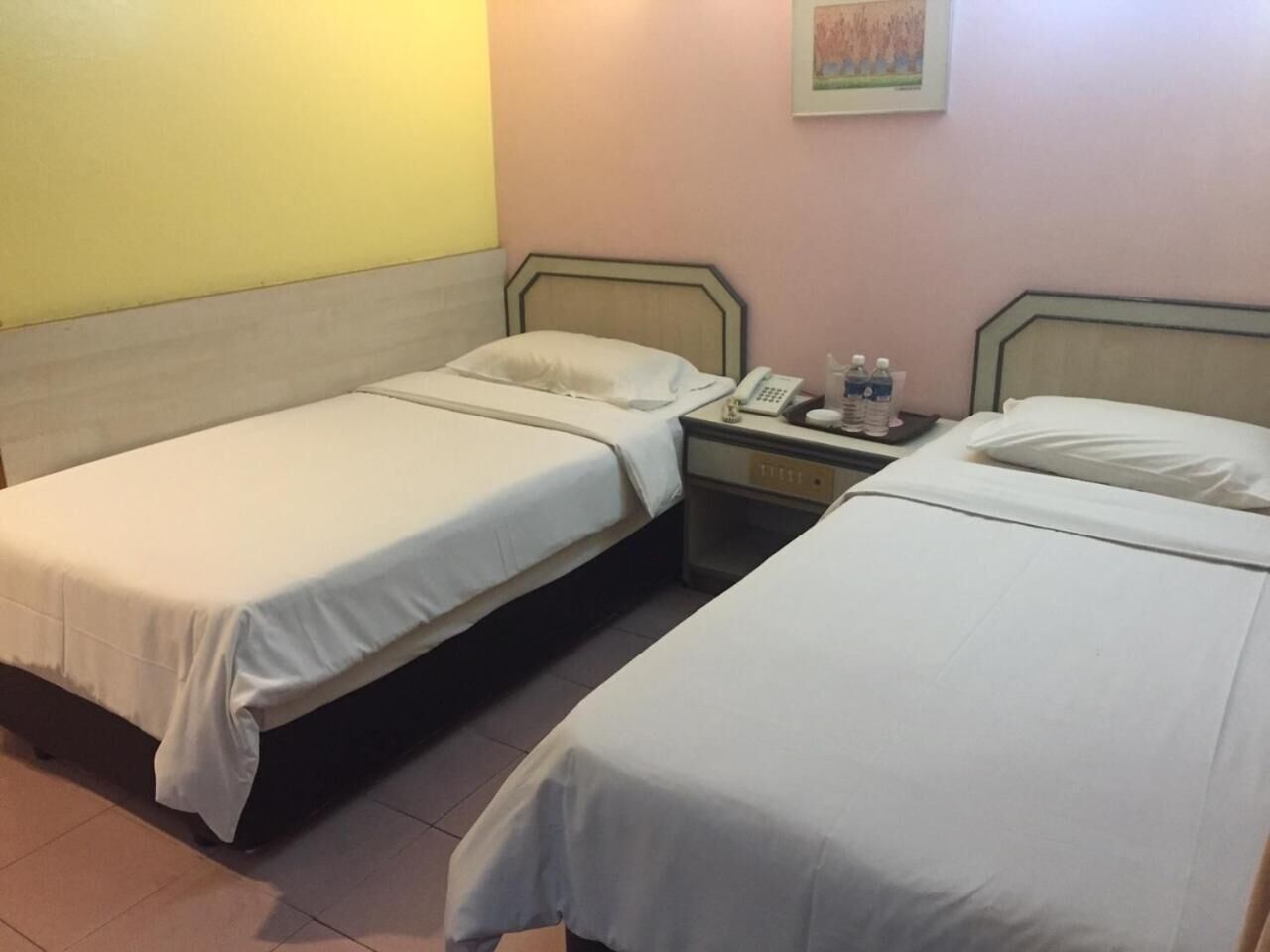 Ein Zimmer mit zwei Einzelbetten, einem Nachttisch mit Lampe, Telefon und einer Wasserflasche.