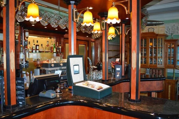 Una zona de bar con una máquina de café, un cuadro enmarcado y una caja de bombones en la barra.