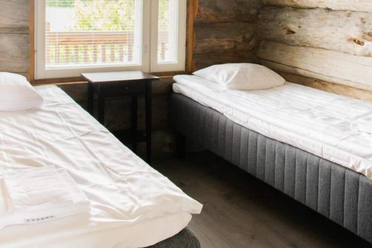 Une chambre de style cabane avec deux lits, une fenêtre avec des rideaux et des poutres apparentes.