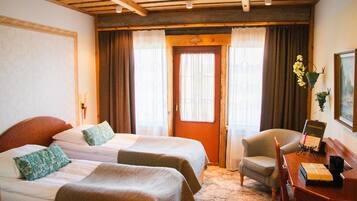 A hotel room with two beds, a wooden ceiling, a chair, a desk, and a door with curtains.