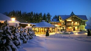 Ein mit Schnee bedecktes Chalet mit mehreren Gebäuden, beleuchteten Fenstern und einer verschneiten Landschaft.