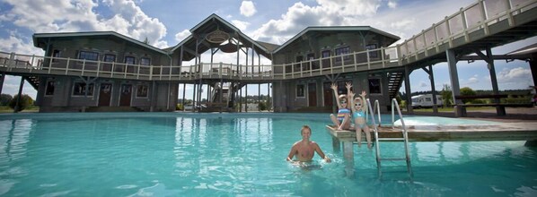 Une piscine avec une terrasse en bois et, au fond, un bâtiment doté d’un toit en verre.