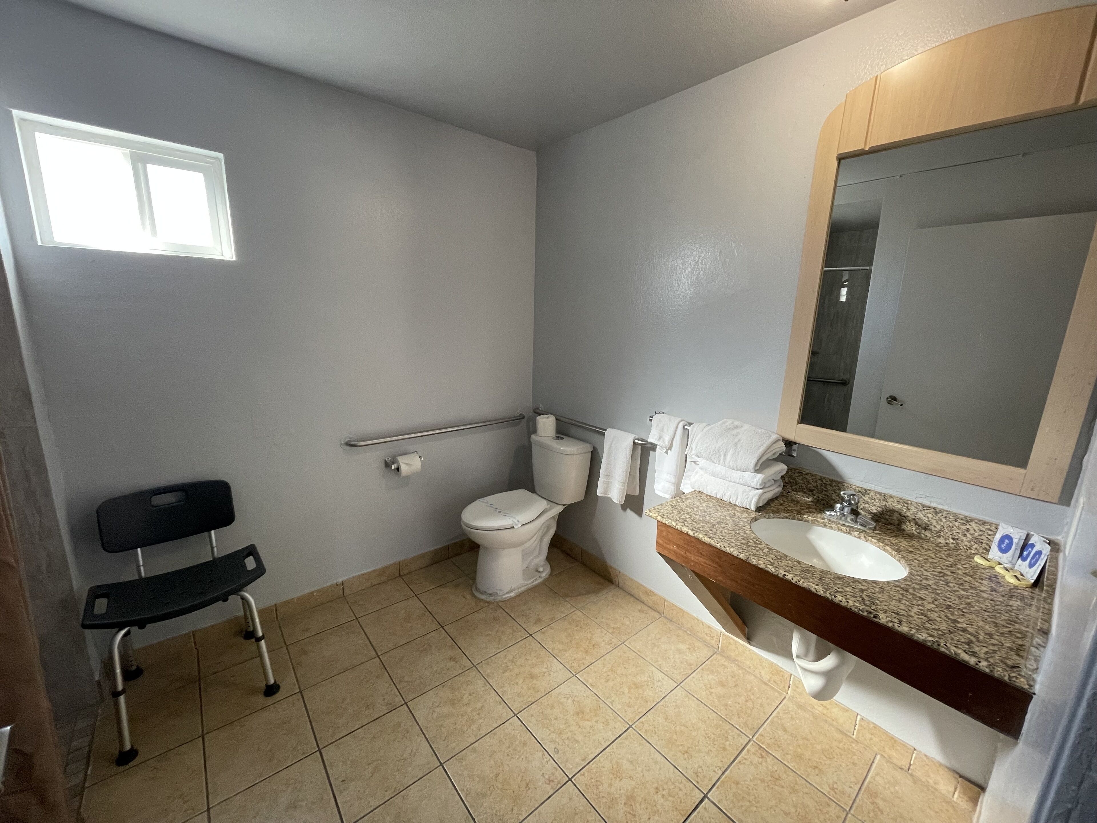 A bathroom with a toilet, sink, mirror, and a wheelchair.
