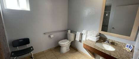 A bathroom with a toilet, sink, mirror, and a wheelchair.