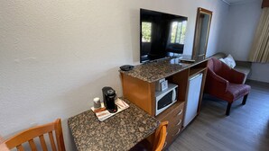 Habitación de hotel compacta con kitchenette, televisión, microondas, cafetera y un sillón rojo.