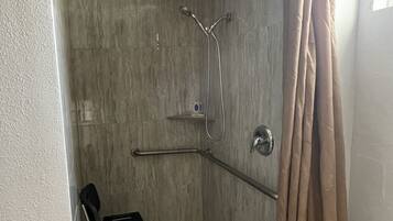A shower area with a showerhead, a handheld shower, and a grab bar.