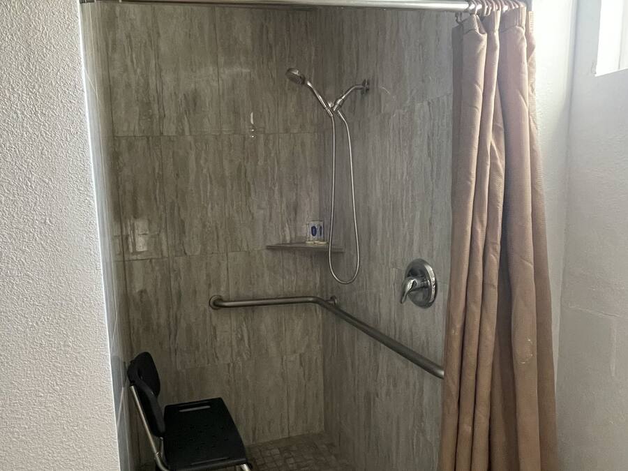 A shower area with a showerhead, a handheld shower, and a grab bar.