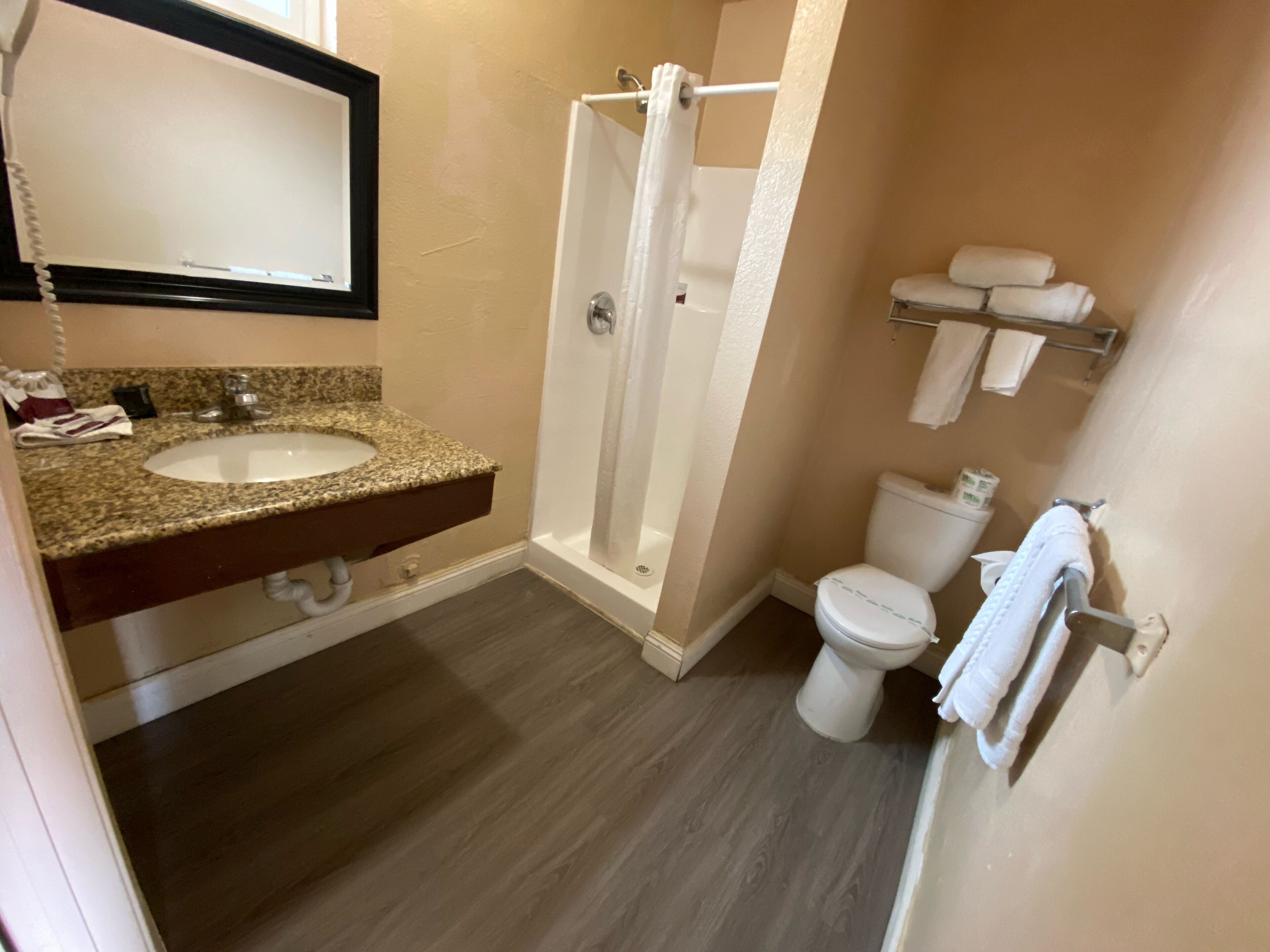 Een badkamer met een wastafel met een granieten blad, een douche, toilet en een handdoekhouder.