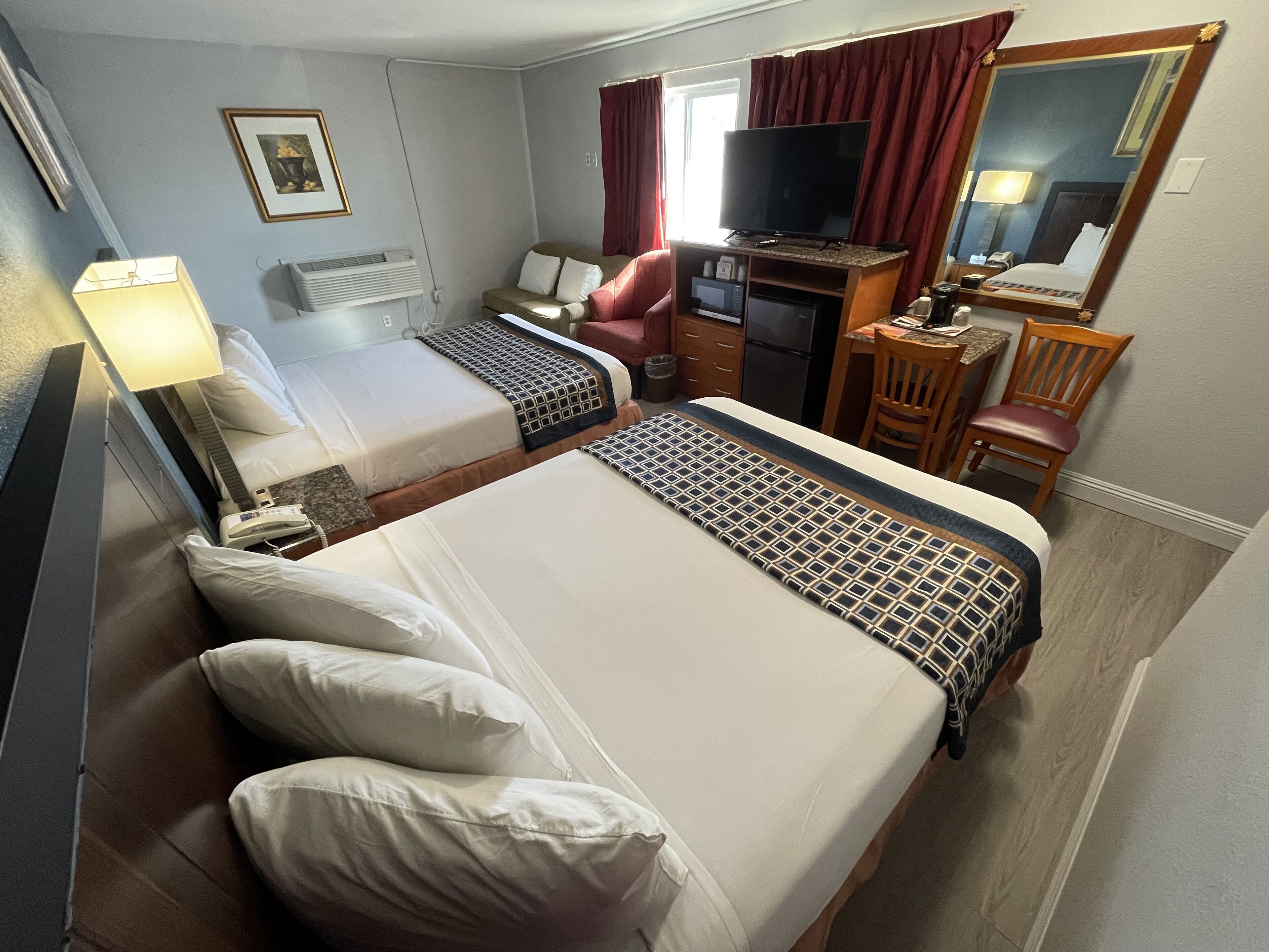 Habitación de hotel con dos camas, un escritorio con computadora, televisor, silla y una mesita.