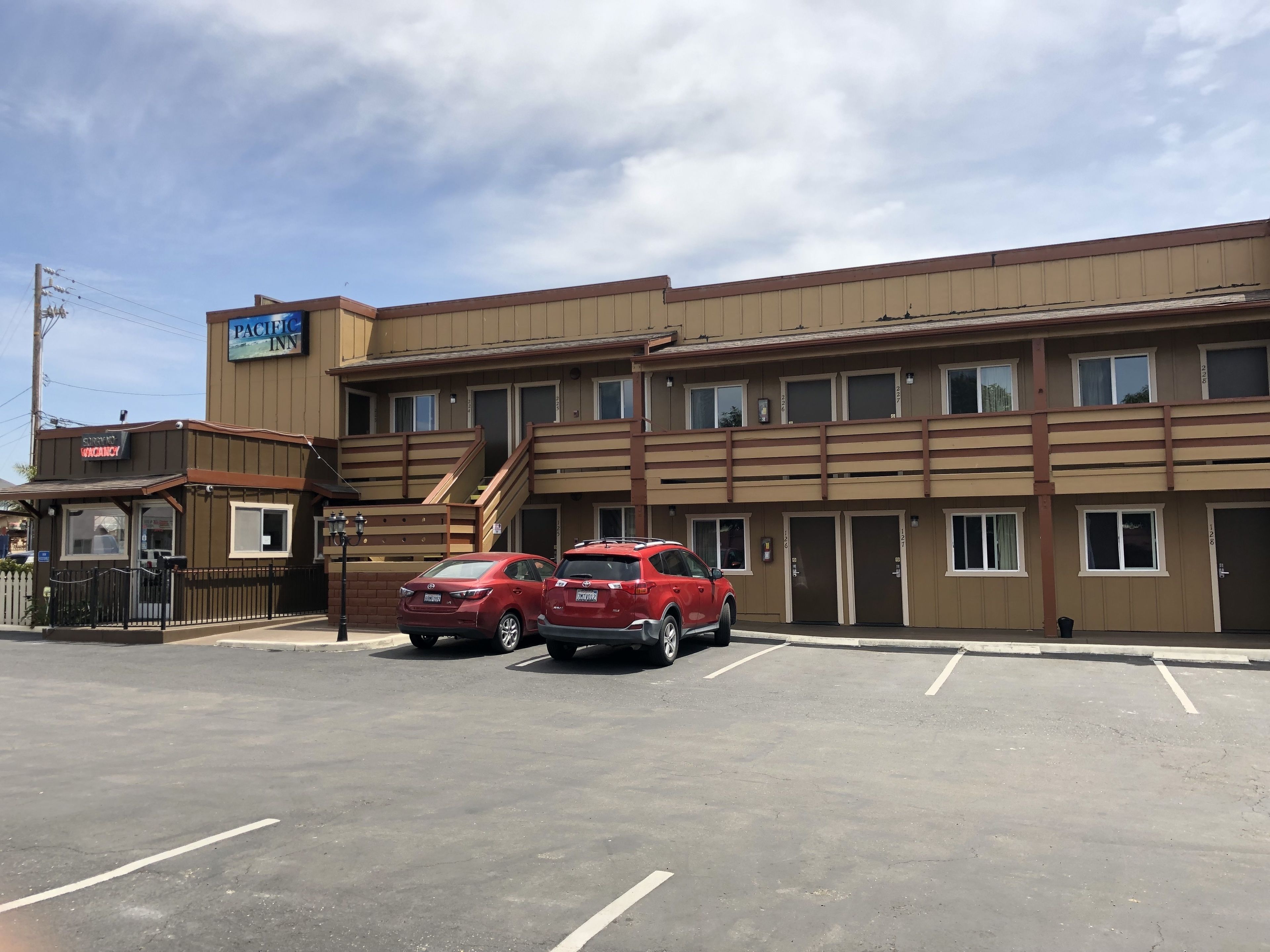 Edificio del Pacific Inn a due piani, con una scala e un parcheggio con due auto rosse.
