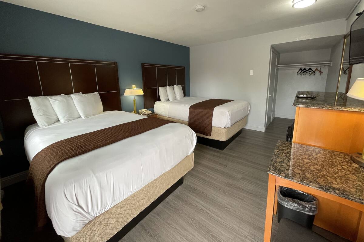 A hotel room with two beds, a desk, a trash bin, and a mirror.