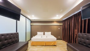 A modern bedroom with a large bed, two sofas, a flat-screen TV, and a sliding door. - Land Royal Residence Pattaya (Pattaya)