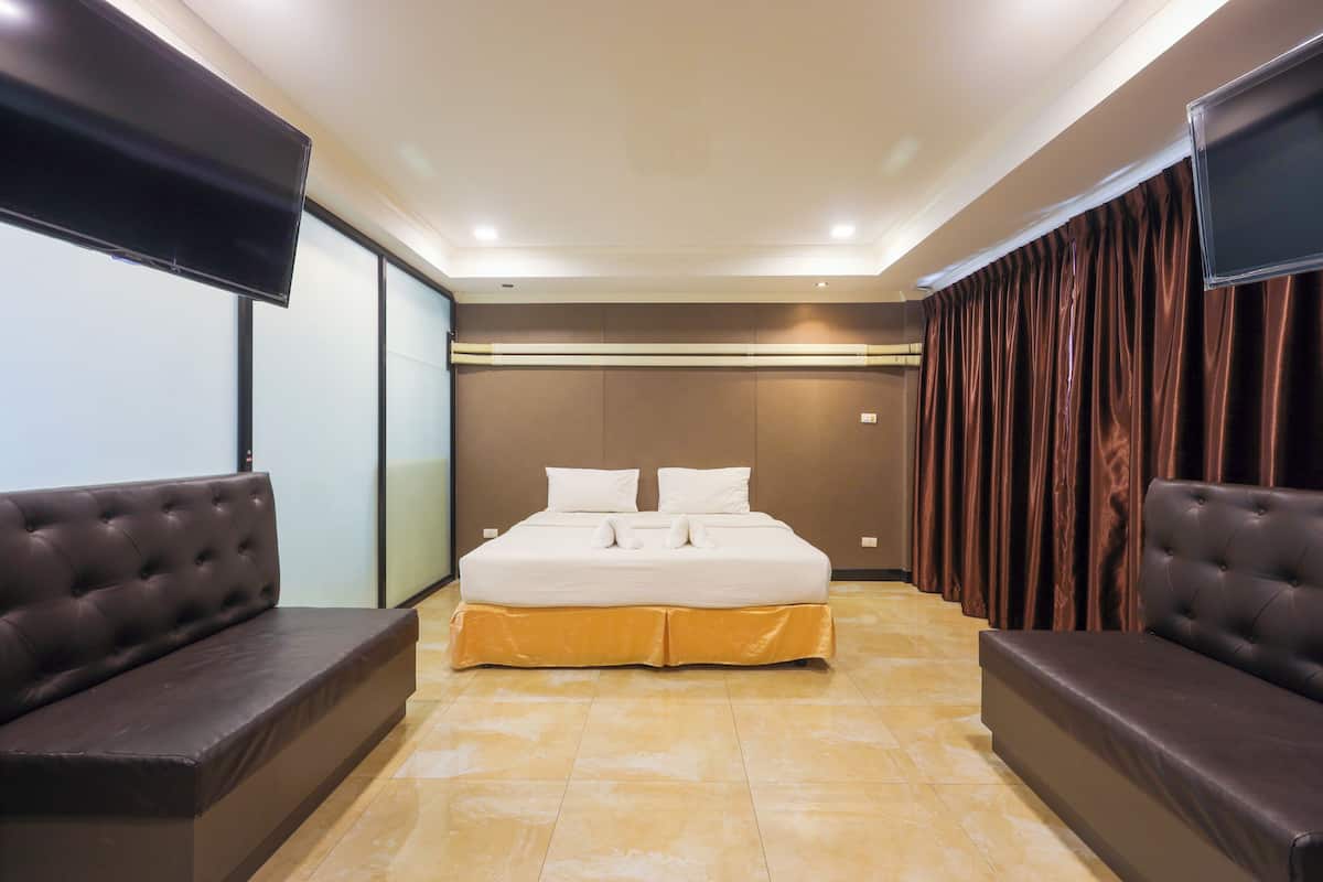 A modern bedroom with a large bed, two sofas, a flat-screen TV, and a sliding door.