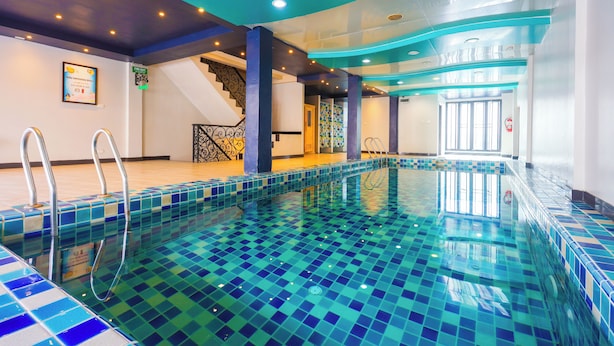 A swimming pool with blue and green mosaic tiles, a staircase with a black railing, and a staircase with a white railing. - Land Royal Residence Pattaya (Pattaya)