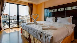 A hotel room with a large bed, a balcony with a view of the city, and a decorative heart-shaped towel on the bed. - Land Royal Residence Pattaya (Pattaya)
