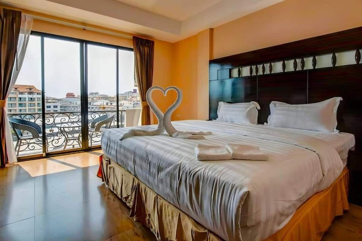 A hotel room with a large bed, a balcony with a view of the city, and a decorative heart-shaped towel on the bed.