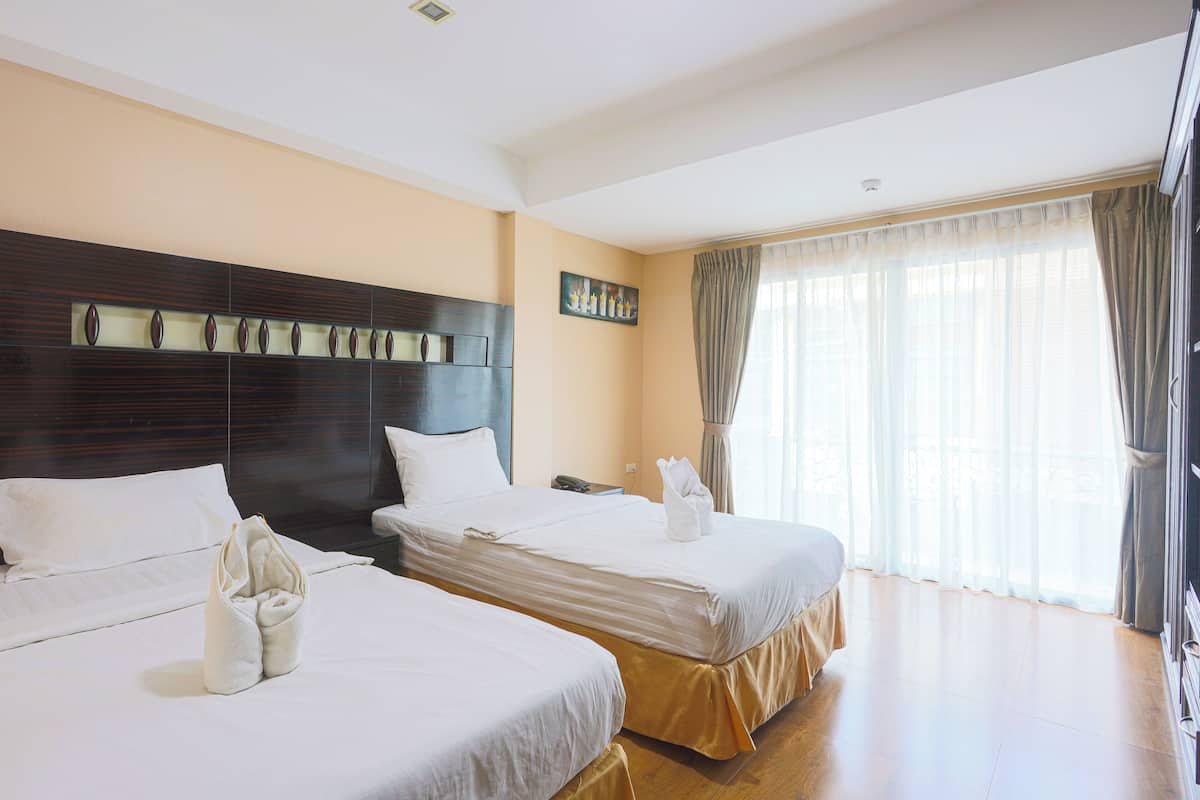 A hotel room with two beds, a wooden headboard, a painting on the wall, and a large window with curtains.