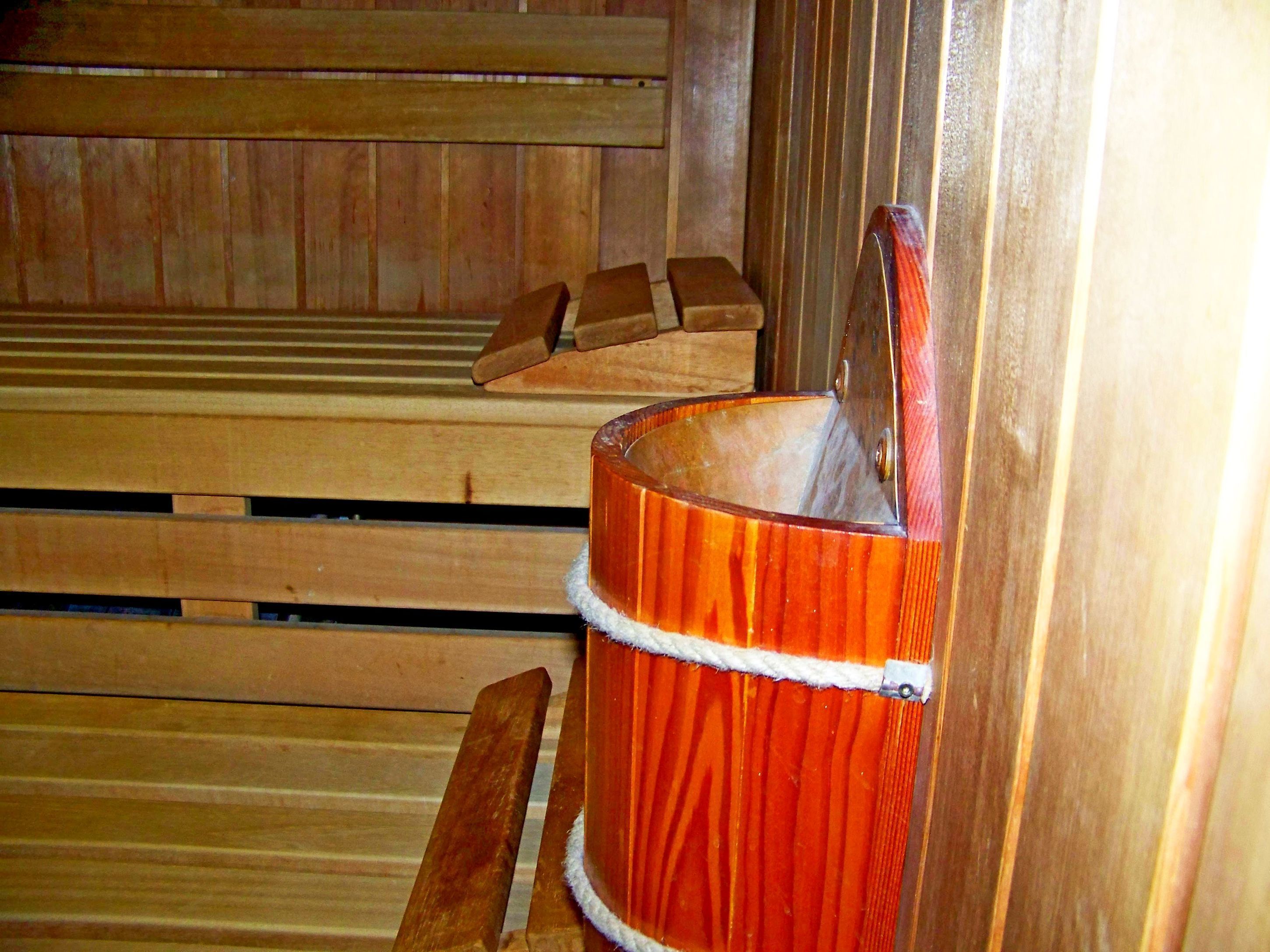 En sauna med træbænke og en træspand med rebhåndtag.