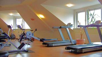Une salle de sport équipée de divers appareils d’exercice, notamment des tapis de course et des vélos d’appartement, dans une pièce dotée de grandes fenêtres et d’un plafond en pente.