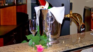 Una zona de bar con una botella de champán en un cubo, dos copas y una rosa en la barra.