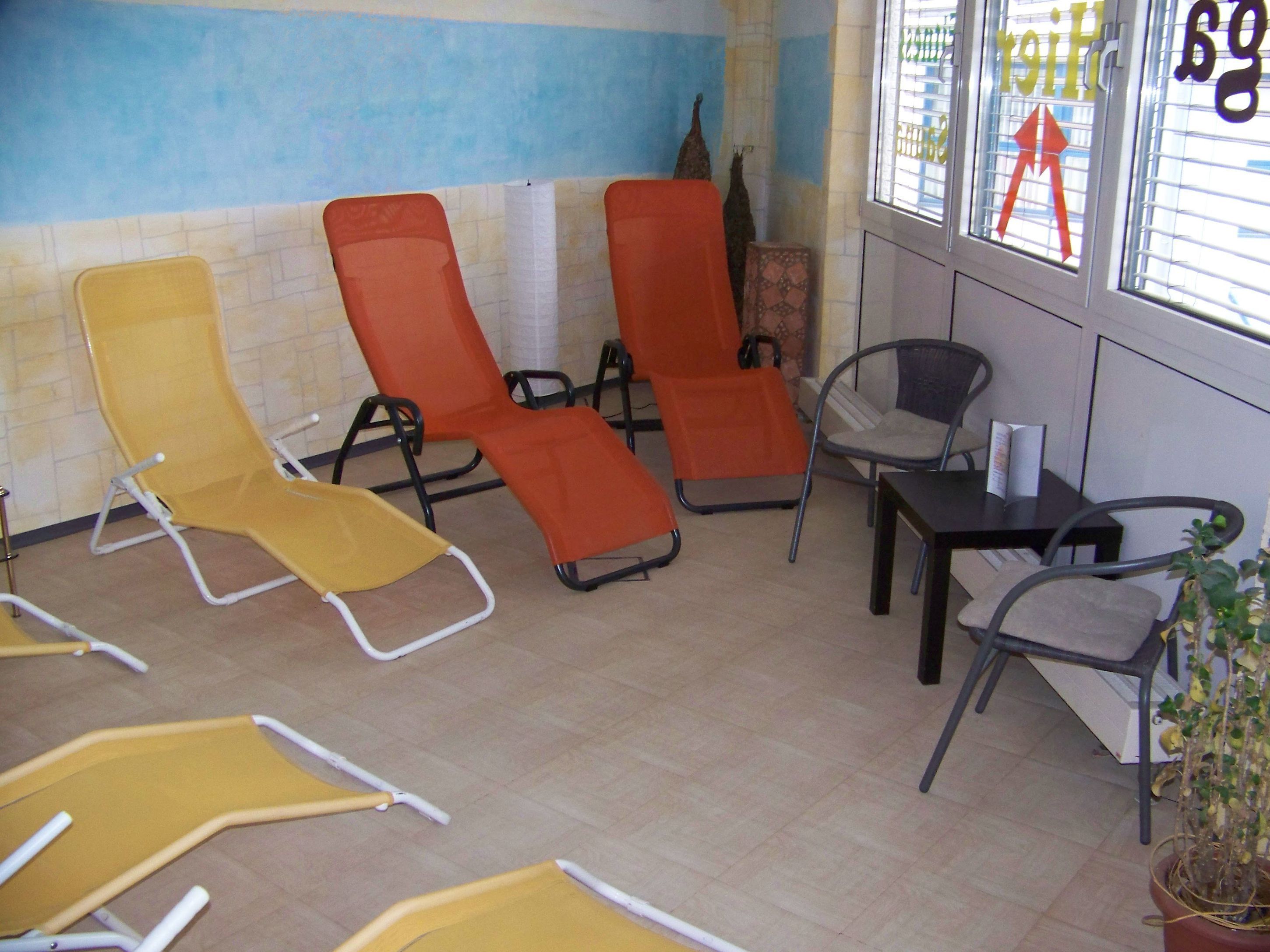 A room with several sun loungers, a small table, and a potted plant.