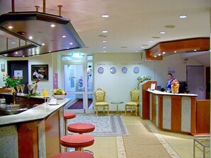 A hotel lobby with a reception desk, bar area, and seating. - Hotel Amadeus ROYAL Berlin (Hoppegarten)