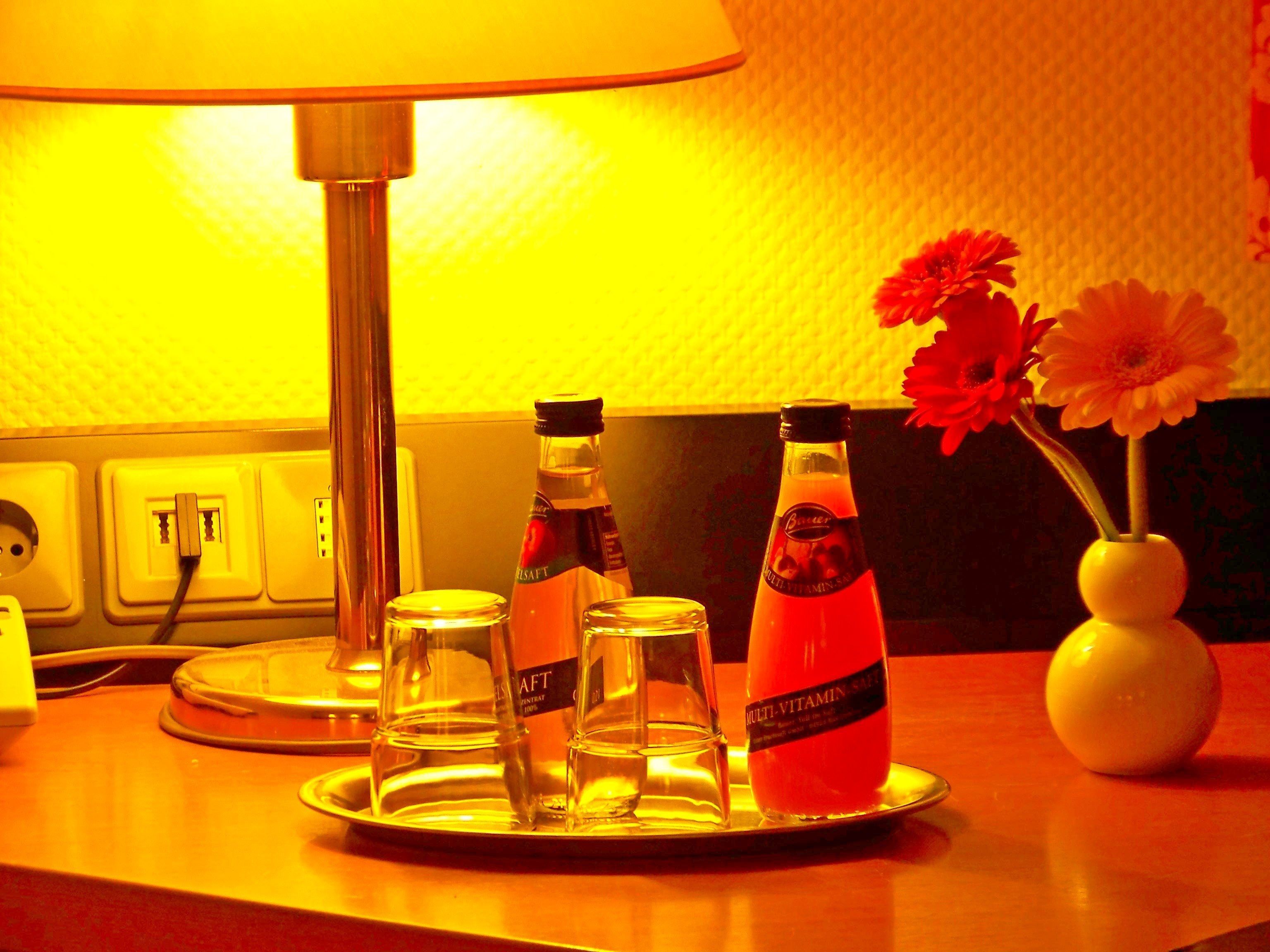 Une table avec une lampe, deux bouteilles étiquetées « SEL MULTIVITAMINÉ », un verre et un vase avec des fleurs.