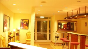 Un hall de hotel con mostrador de recepción, zona de bar con taburetes, un espejo grande y obras de arte en las paredes.