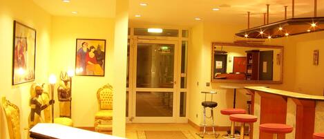 A hotel lobby with a reception desk, bar area with stools, a large mirror, and artwork on the walls.