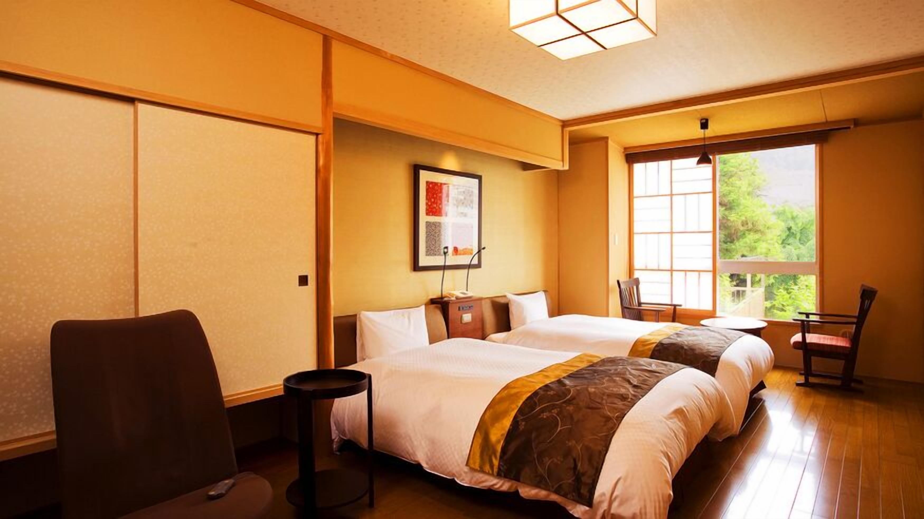 Une chambre d’hôtel avec deux lits, une petite table, une chaise et une fenêtre donnant sur un paysage agréable.