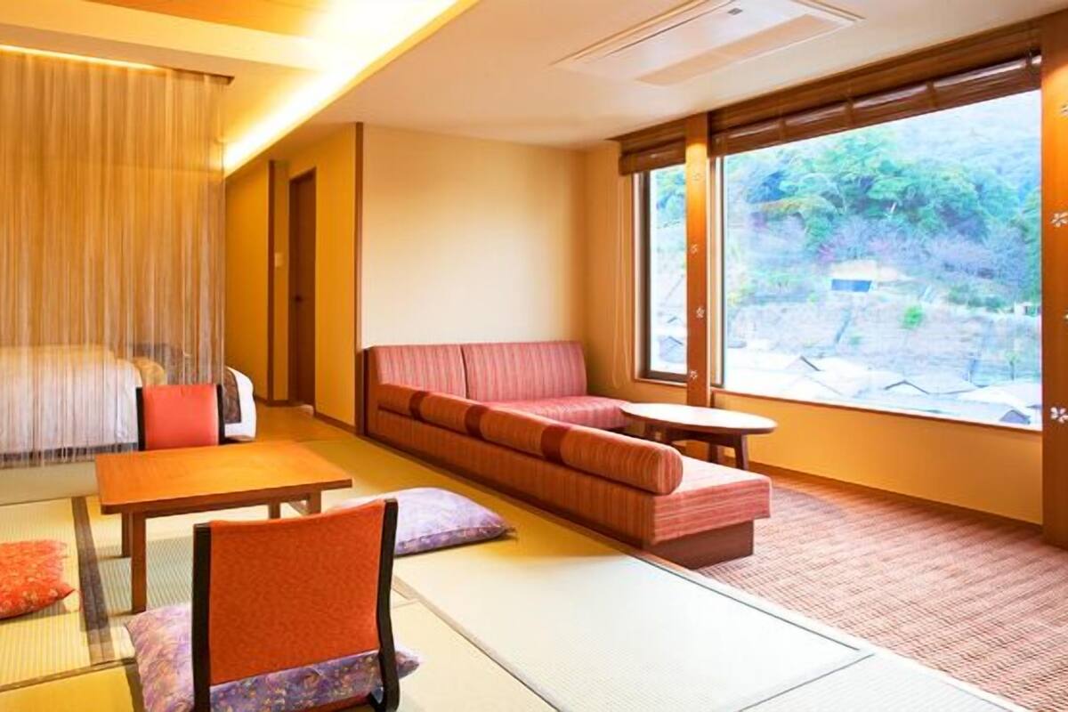 A traditional Japanese-style room with tatami flooring, a low table, a sofa, and a bed with a canopy.