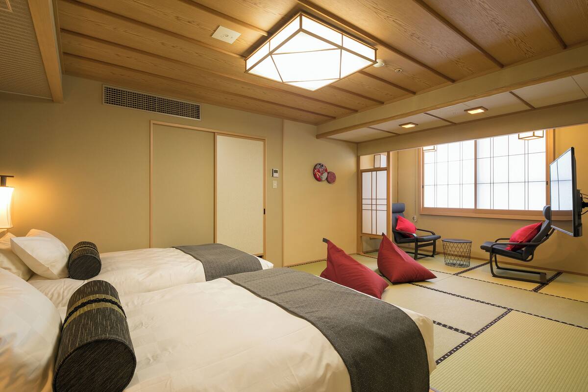 A traditional Japanese-style room with tatami flooring, two beds with pillows, a tatami mat table, and a sliding door.