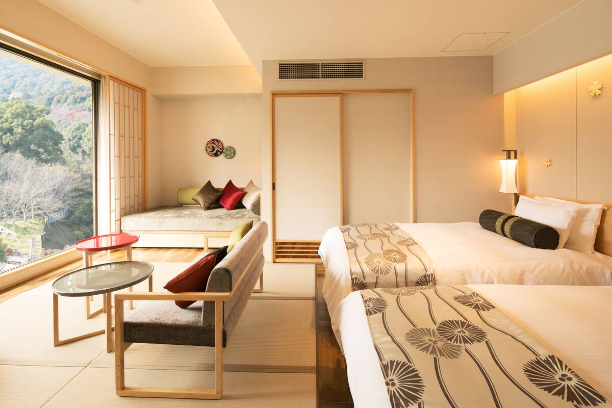 A hotel room with a bed, a sofa, a small table, and a view of the outdoors.