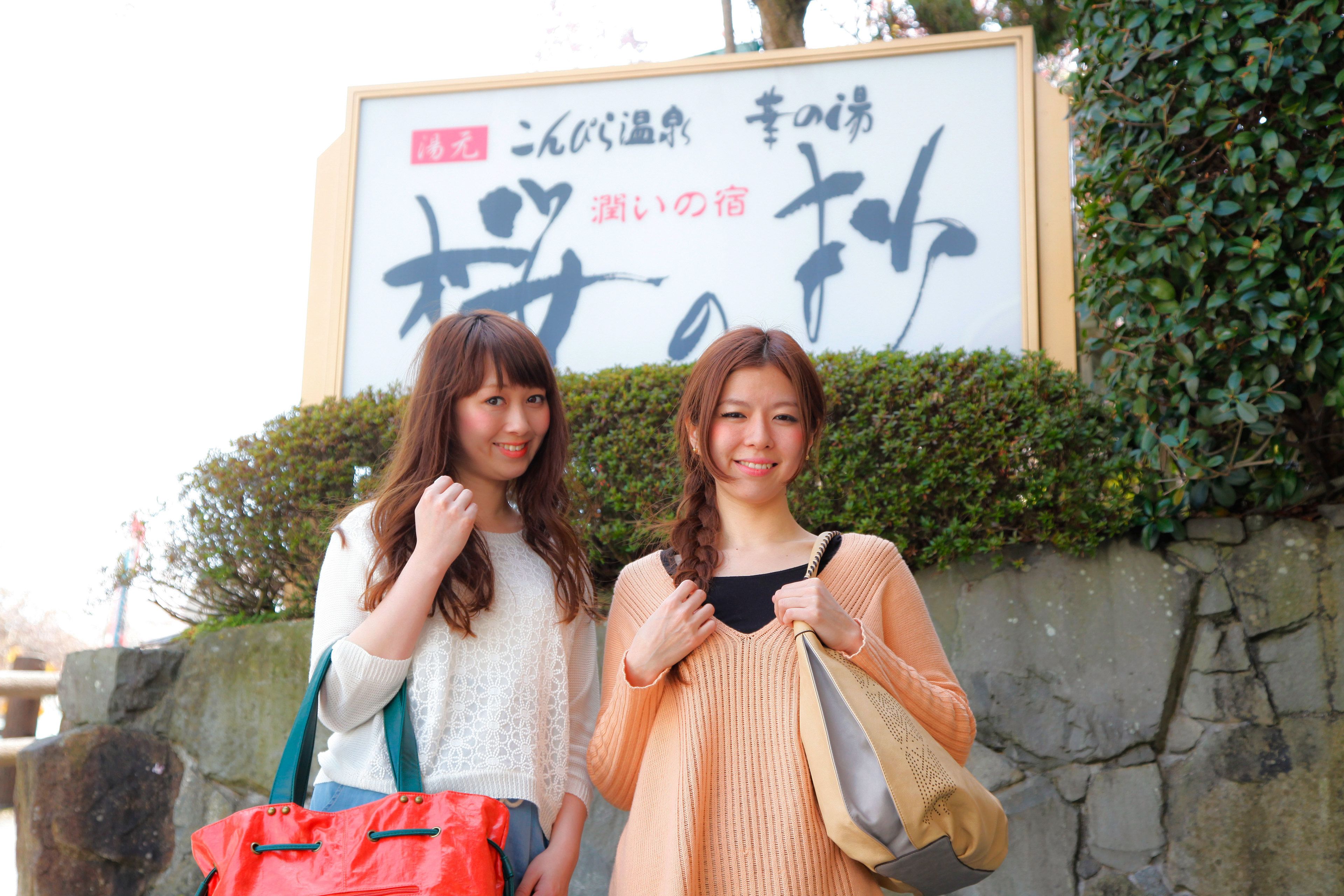 Two women standing in front of a sign with Japanese characters.