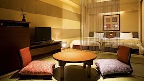 A traditional Japanese-style room with tatami flooring, a low wooden table, two tatami mats with cushions, a television, and a bed with a canopy. - Kotohira Grand Hotel Sakuranosho (Kotohira)