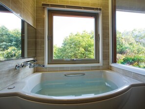 A bathroom with a large bathtub, a window with a view of trees, and a mirror on the wall.