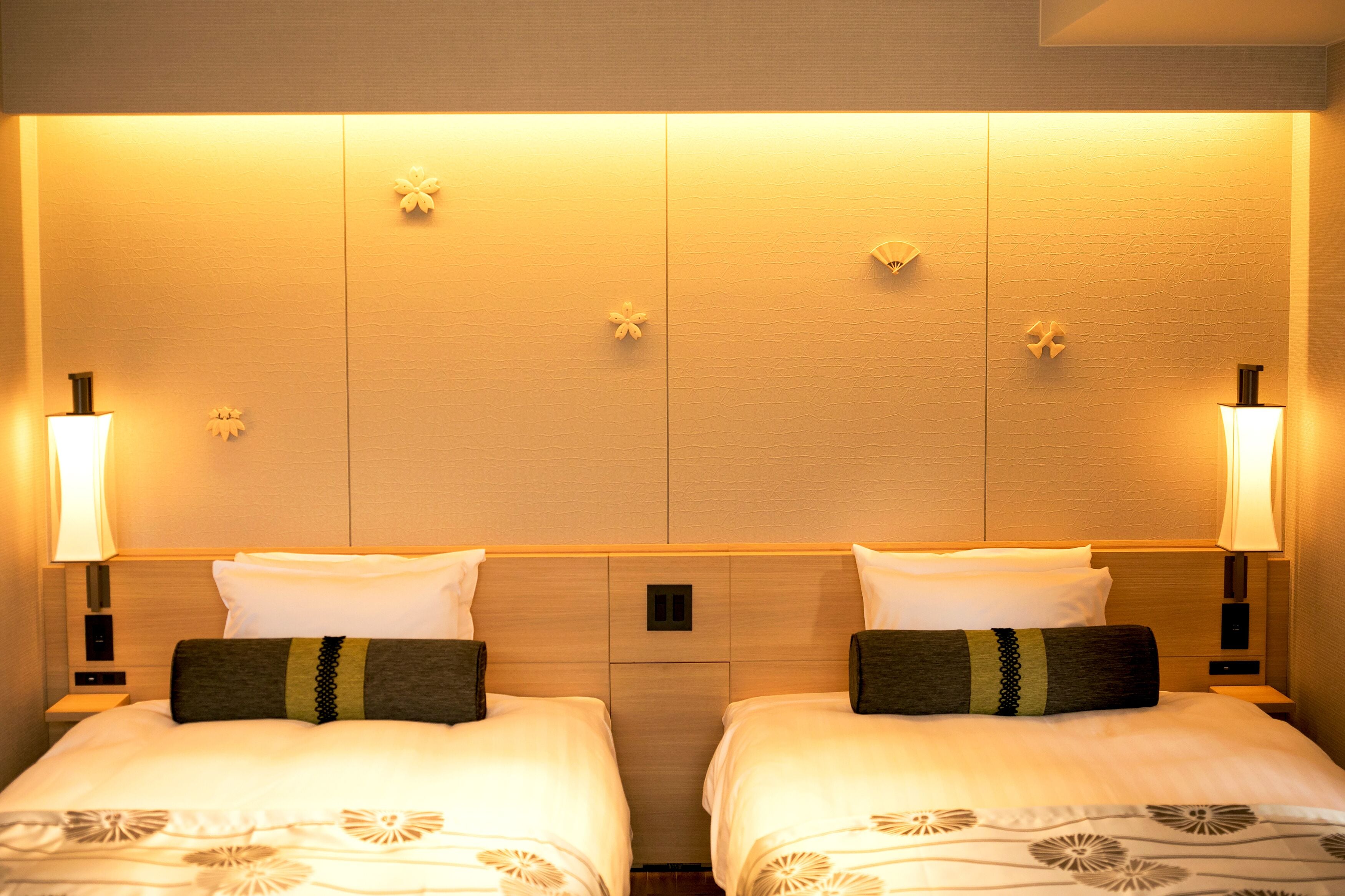A hotel room with two beds, each with a pillow and a bedside table.