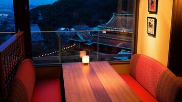 A room with a wooden table and red cushioned seating, a window with a view of traditional buildings, and framed pictures on the wall.